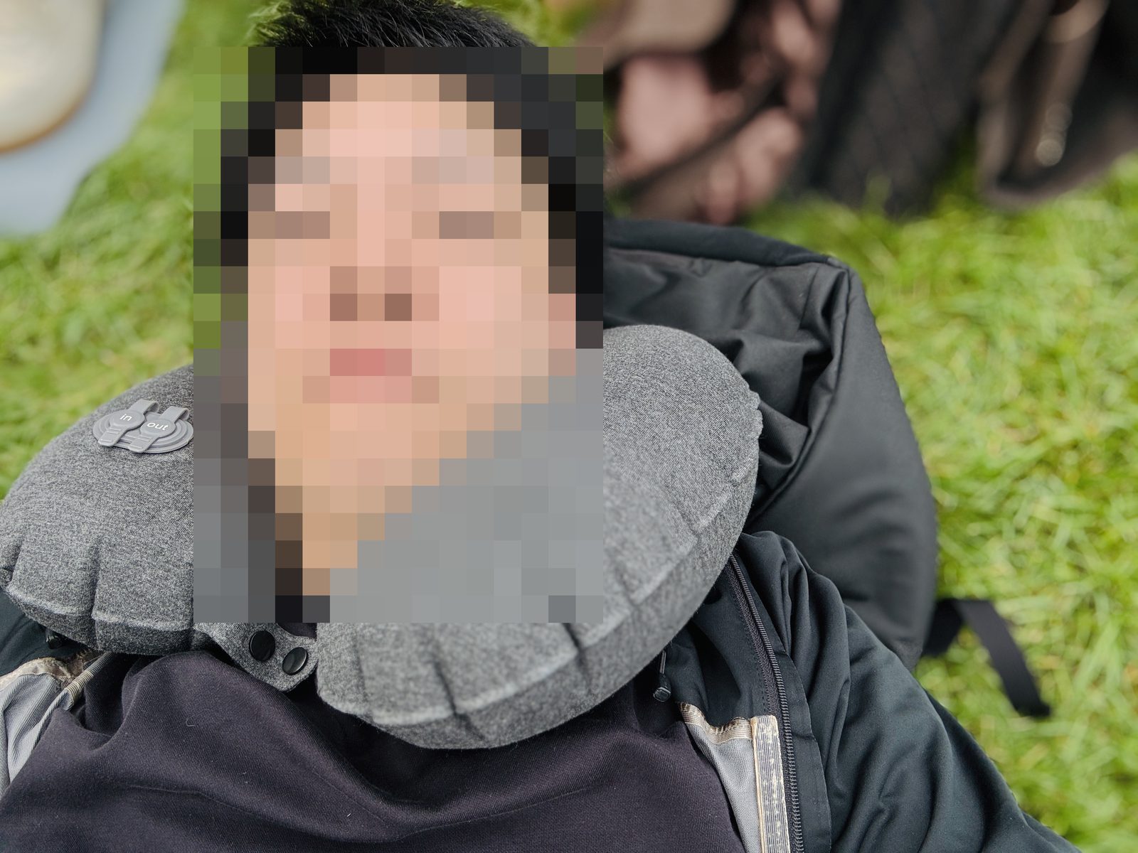 公園の芝生でネックピローを使って休憩している写真 顔はモザイク加工
